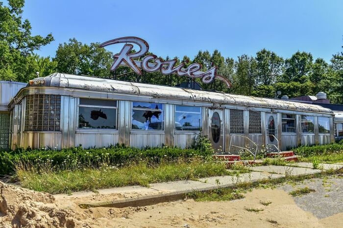 Overgrown plants surround an abandoned diner, showcasing nature reclaiming civilization.