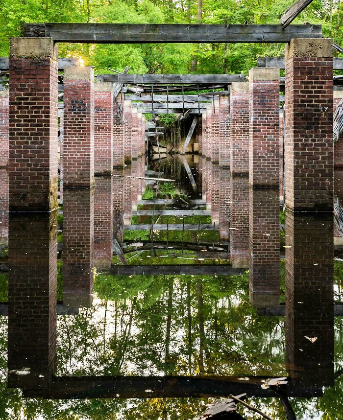 Abandoned brick structure with water reflection, surrounded by greenery, illustrating nature reclaiming civilization.