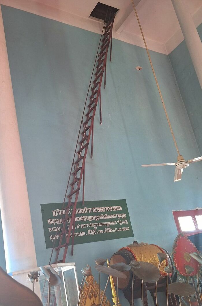 Steep and narrow "death stairs" leading to a ceiling opening in a museum setting with artifacts displayed below.