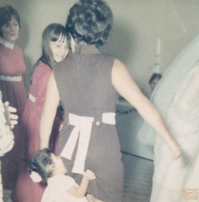 Young girl clinging to woman’s dress in awkward family photo capturing a sweet, candid moment at a gathering.