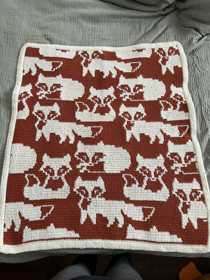 Crochet blanket featuring a repeating fox pattern in brown and white, showcasing detailed crochet craftsmanship.