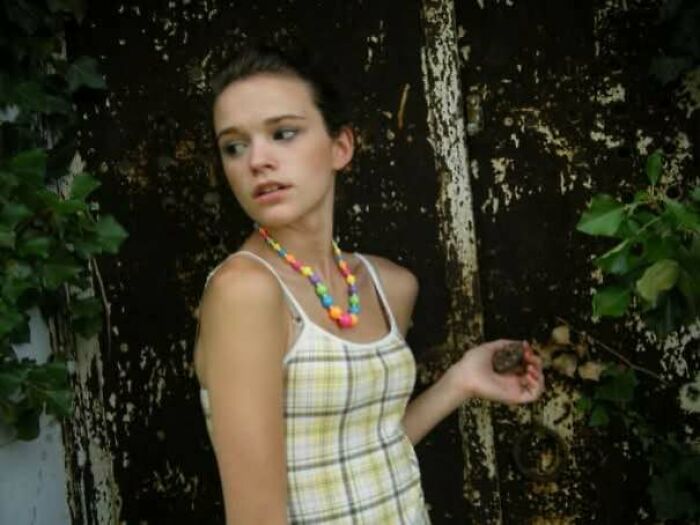 Teen girl in a plaid dress and colorful necklace posing in front of a weathered door, reflecting a regrettable past moment.