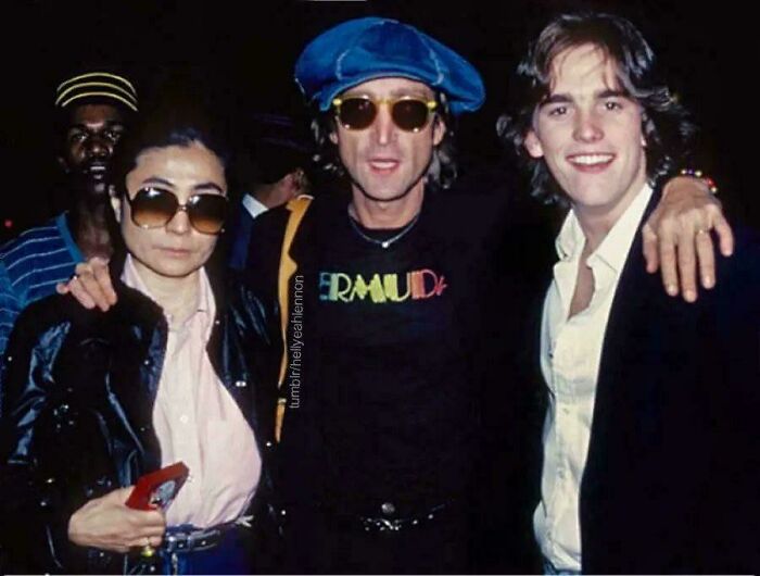 Three people in 70s attire, one wearing sunglasses and a blue cap, capturing a moment of interest.