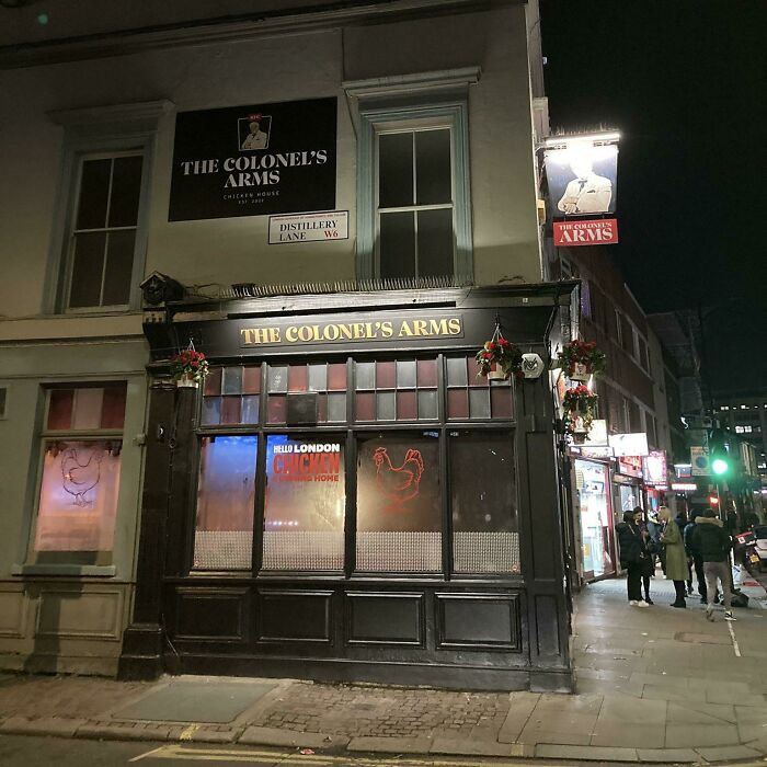 "The Colonel's Arms pub exterior at night, glowing under streetlights, something interesting and unique."