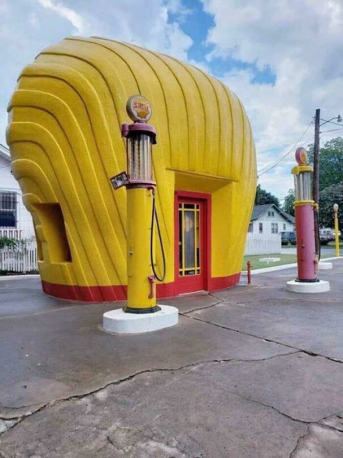Yellow building shaped like a giant seashell with vintage gas pumps in front, showing something interesting.