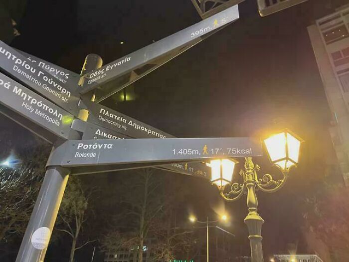 Street signs with distances in meters and calories at night, near a vintage lamp.