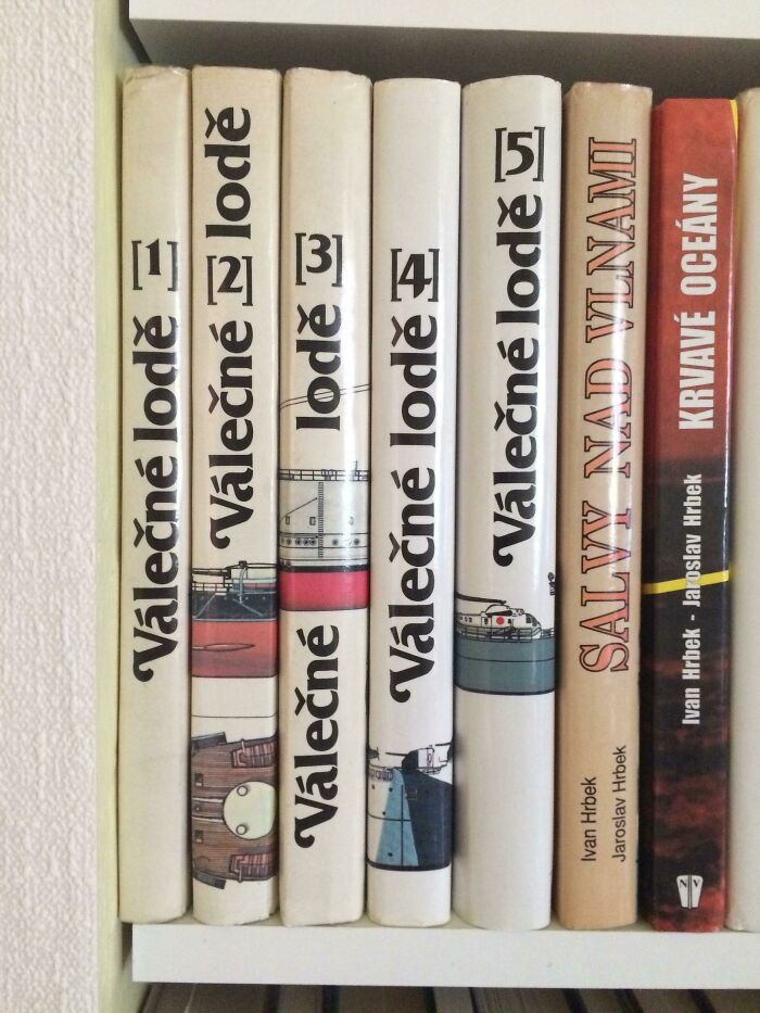 Bookshelf with poorly-written-designed books, featuring white and colorful spines with illustrations and text in a foreign language.