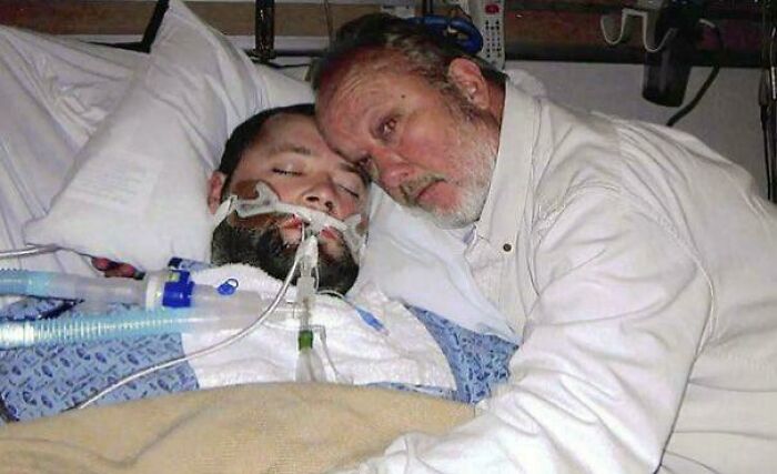 Man lying in hospital bed with breathing tube, another man leaning close in a touching, emotional moment depicting strange Earth events.