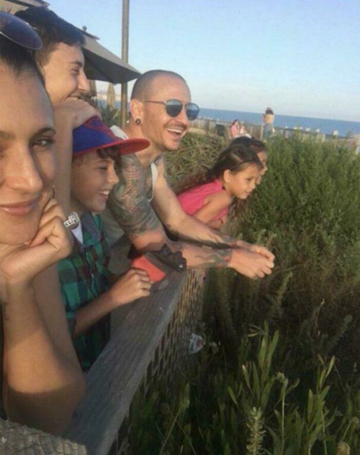 A group of people smiling and looking over a railing at greenery near the ocean on a strange Earth landscape.