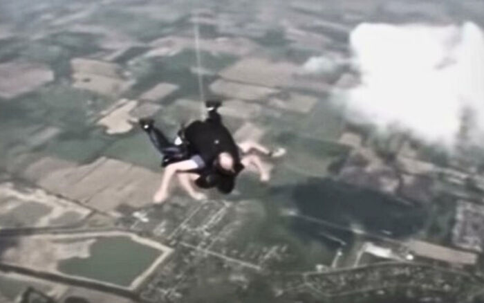 Two people skydiving over a patchwork of fields and clouds, showcasing a strange Earth adventure moment.