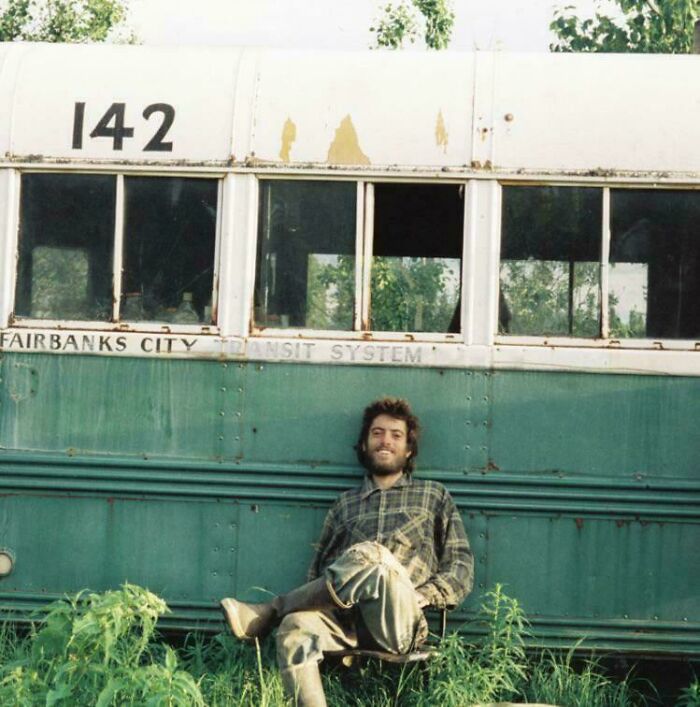 Man sitting in front of an abandoned bus in the wilderness, symbolizing bizarre and unsettling events around the world.