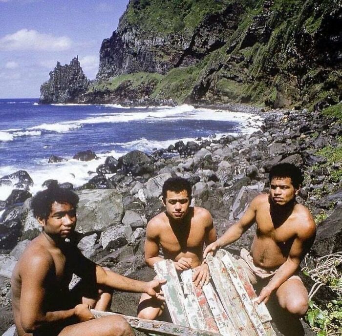 Three men sitting on a rocky shore near waves and cliffs, illustrating strange Earth natural and cultural happenings.