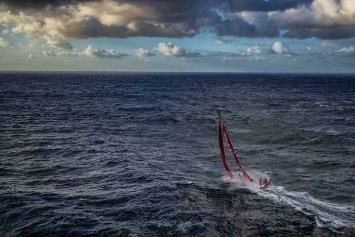 A small sailboat navigating rough ocean waters under a cloudy sky, showcasing strange Earth phenomena.