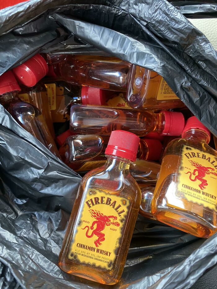 Small Fireball cinnamon whisky bottles discarded inside a black trash bag, capturing insane workplace moments.