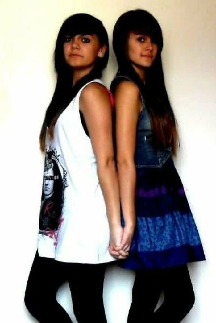 Two young women holding hands standing back to back in casual clothes in a regrettable past photo cringe moment.