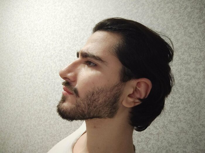 Young man with fierceflow beautiful hair, styled back, showing sharp profile against a textured light background.