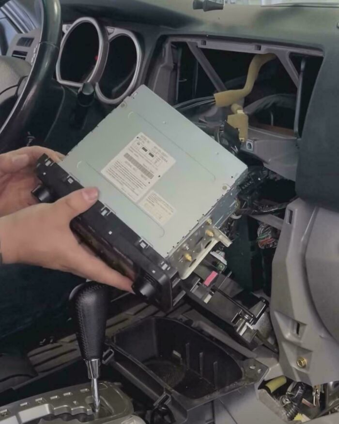 Hands installing a 1990s car stereo into a vehicle dashboard.
