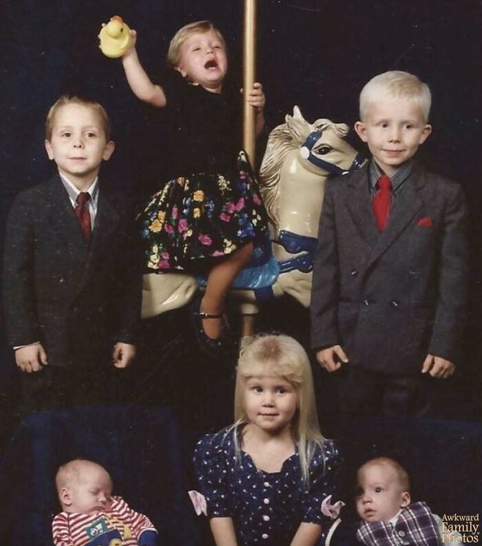 Group of children posing for an awkward family photo with one child crying on a carousel horse, capturing sweet moments.