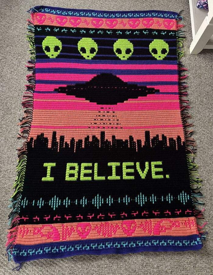 Crochet blanket with alien heads, UFO, city skyline, and I BELIEVE text featuring vibrant colors and detailed patterns.