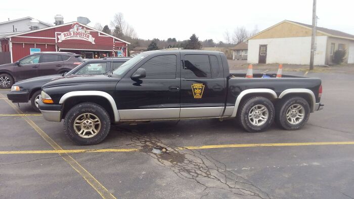 Black six-wheeled pickup truck parked outside a diner, showcasing ingenious redneck engineer vehicle modification.