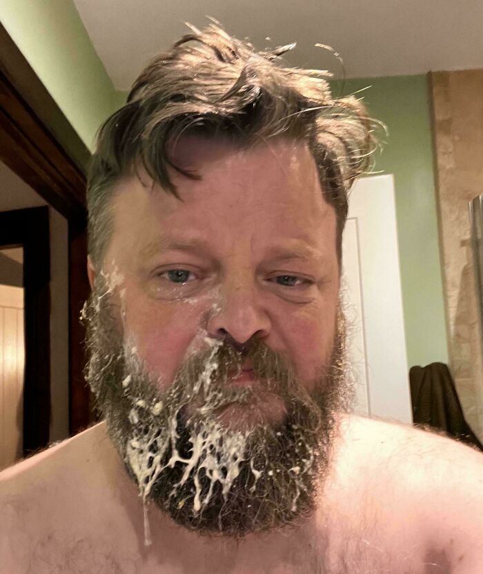 Bearded dad with messy face wearing a humorous expression, showing a relatable parenting moment at home.