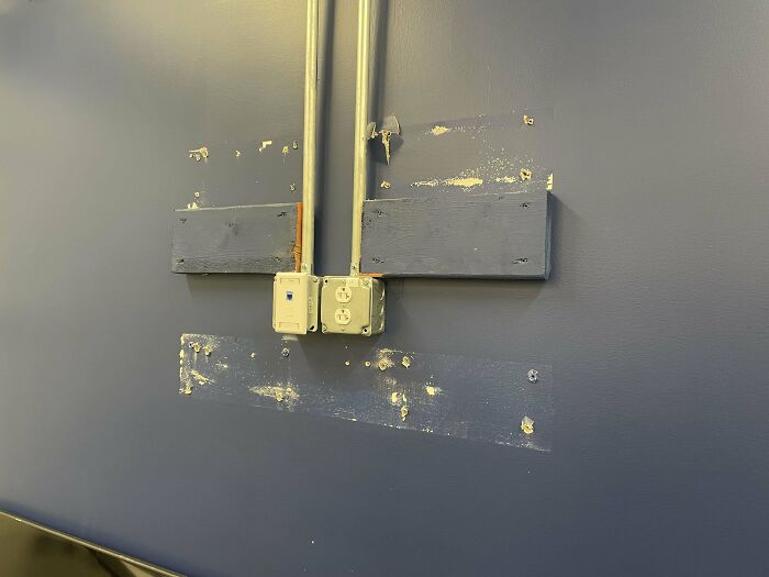 Wall with old mounting marks and electrical outlets showing a tech support workspace that feels unfinished and unprofessional.