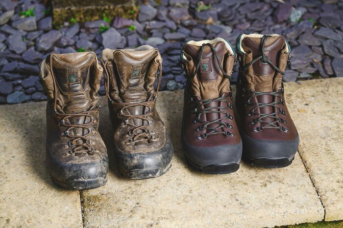 Two pairs of hiking boots, one old and worn, the other new, on a stone path. An example of a Buy It For Life purchase.