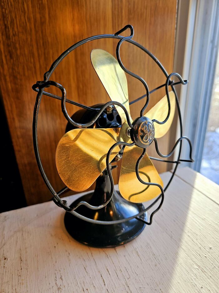 A vintage GE fan with shiny brass blades and a black casing on a rustic white surface. A true Buy It For Life item.