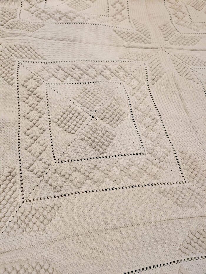 Close-up of an intricate crochet masterpiece blanket with textured patterns and detailed stitch work in a neutral color.