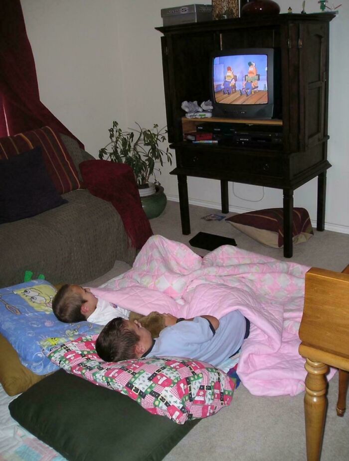 Kids watching cartoons on an old TV, wrapped in blankets, evokes 2000s nostalgia.
