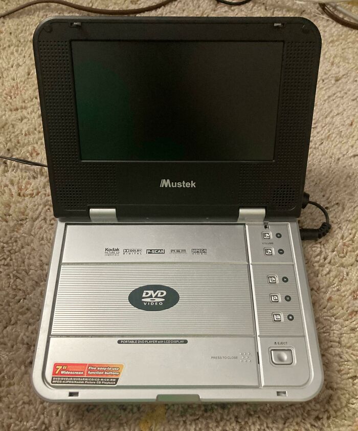Portable DVD player from the 2000s on a carpeted floor, showcasing nostalgic tech design.