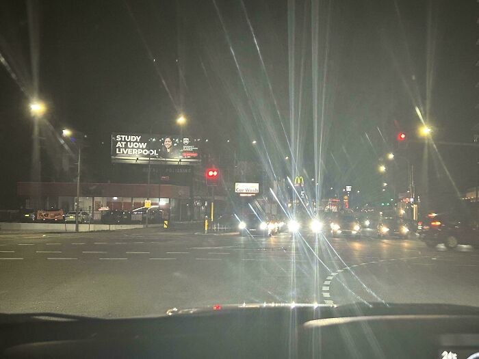 Nighttime street view in Australia with lit billboards and headlights illuminating the road.