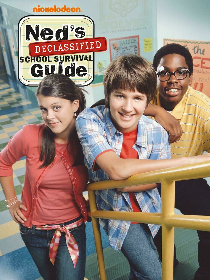 Three teens from a 2000s Nickelodeon show pose together in a school hallway, smiling and leaning on a railing.