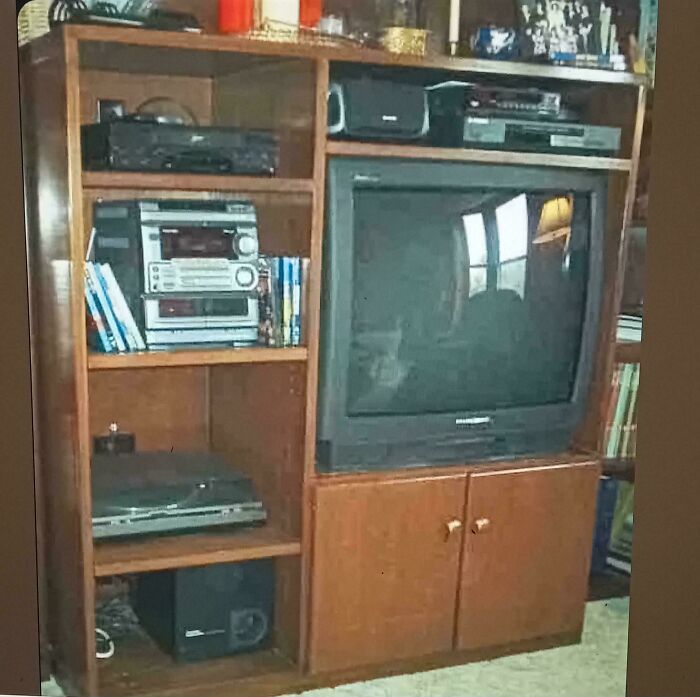 2000s nostalgic entertainment unit with a CRT TV, DVD player, stereo system, and VHS tapes on a wooden shelf.
