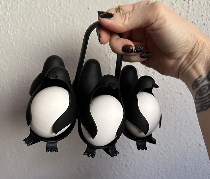 Hand holding clever invention: a penguin-shaped egg holder carrying three eggs.