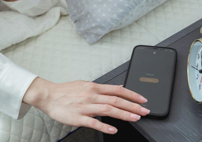 Hand reaching for a smartphone on bedside table to turn off alarm, showcasing brilliant life hacks for a smoother morning routine.