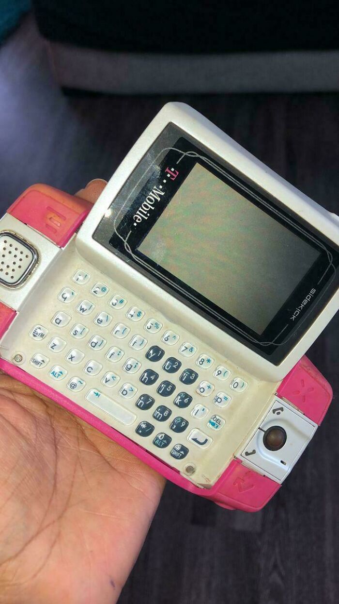 2000s nostalgia: a hand holding a vintage pink T-Mobile Sidekick slider phone with a keyboard.