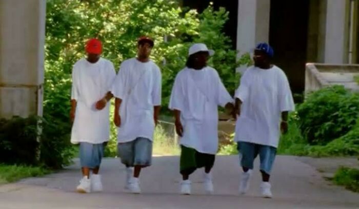 Four people in oversized 2000s fashion, wearing baggy jeans and white tees, walk outdoors.