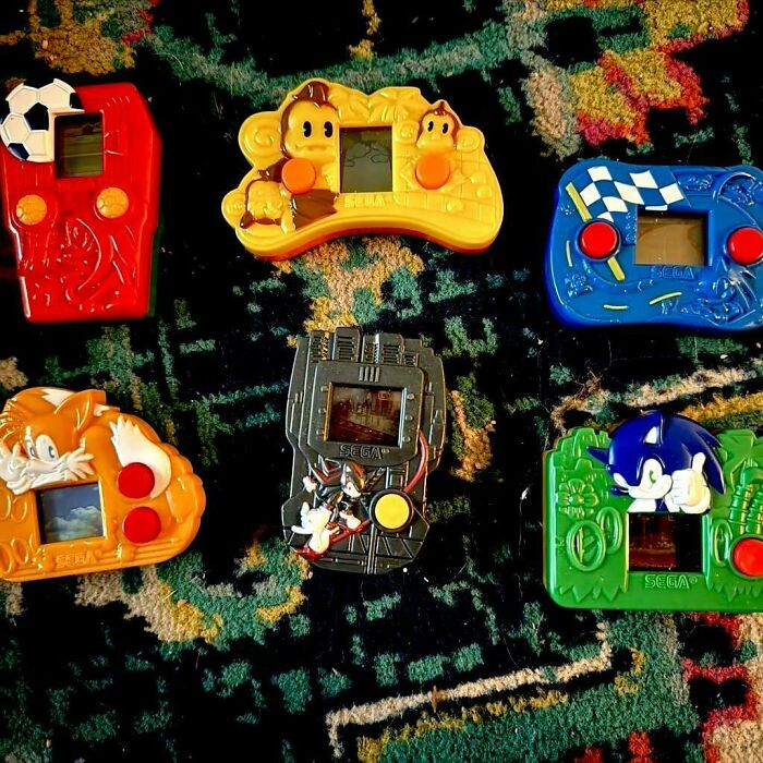 Colorful handheld games from the 2000s featuring characters like Sonic and others, arranged on a patterned carpet.