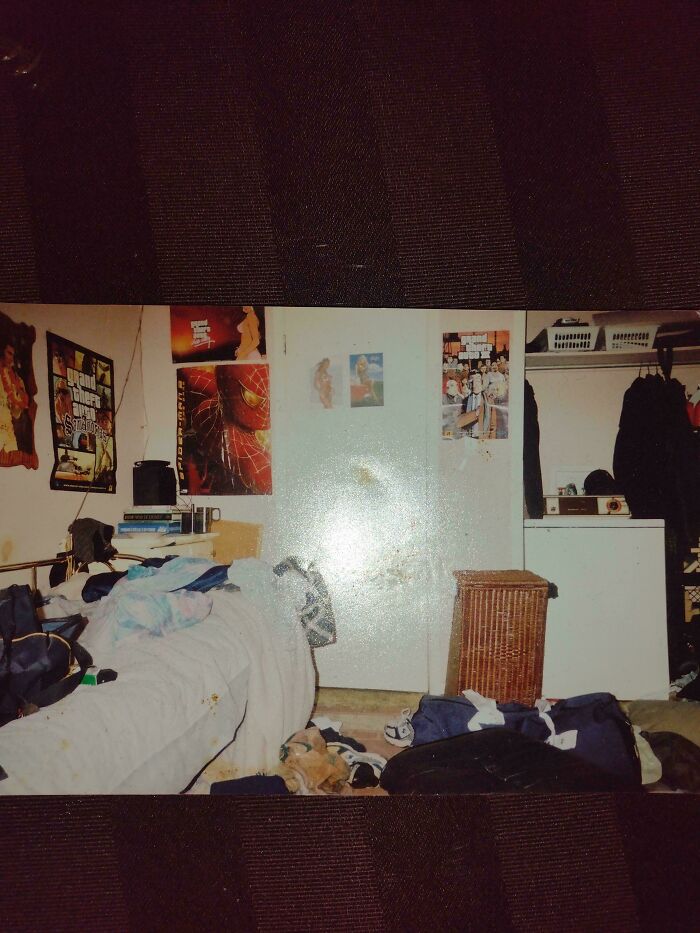 Messy 2000s bedroom with posters, cluttered bed, and clothes on the floor.