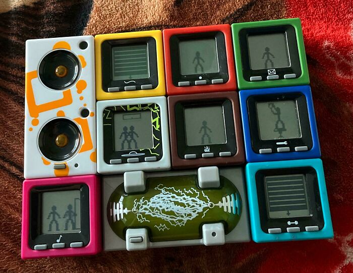 Collection of 2000s era pixelated electronic screen toys with colorful cases on a patterned fabric.