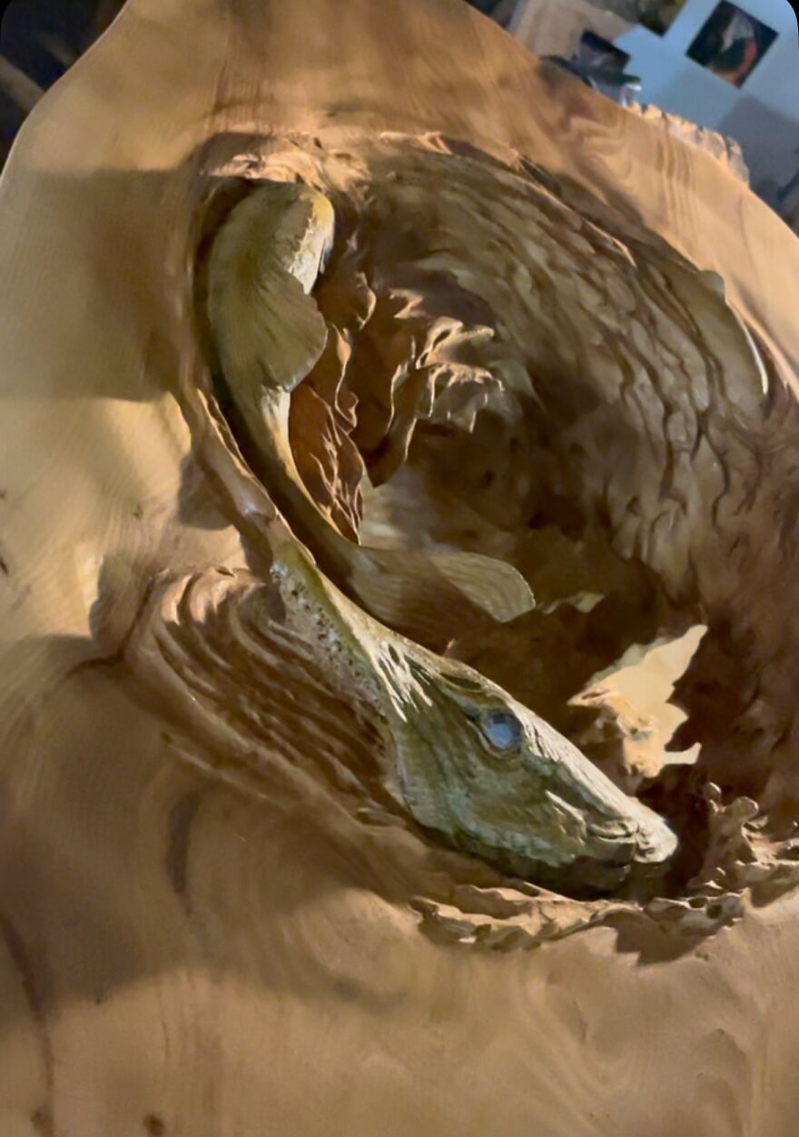 Chainsaw artist's intricate sculpture of a fish emerging from a log, showcasing detailed carving techniques.
