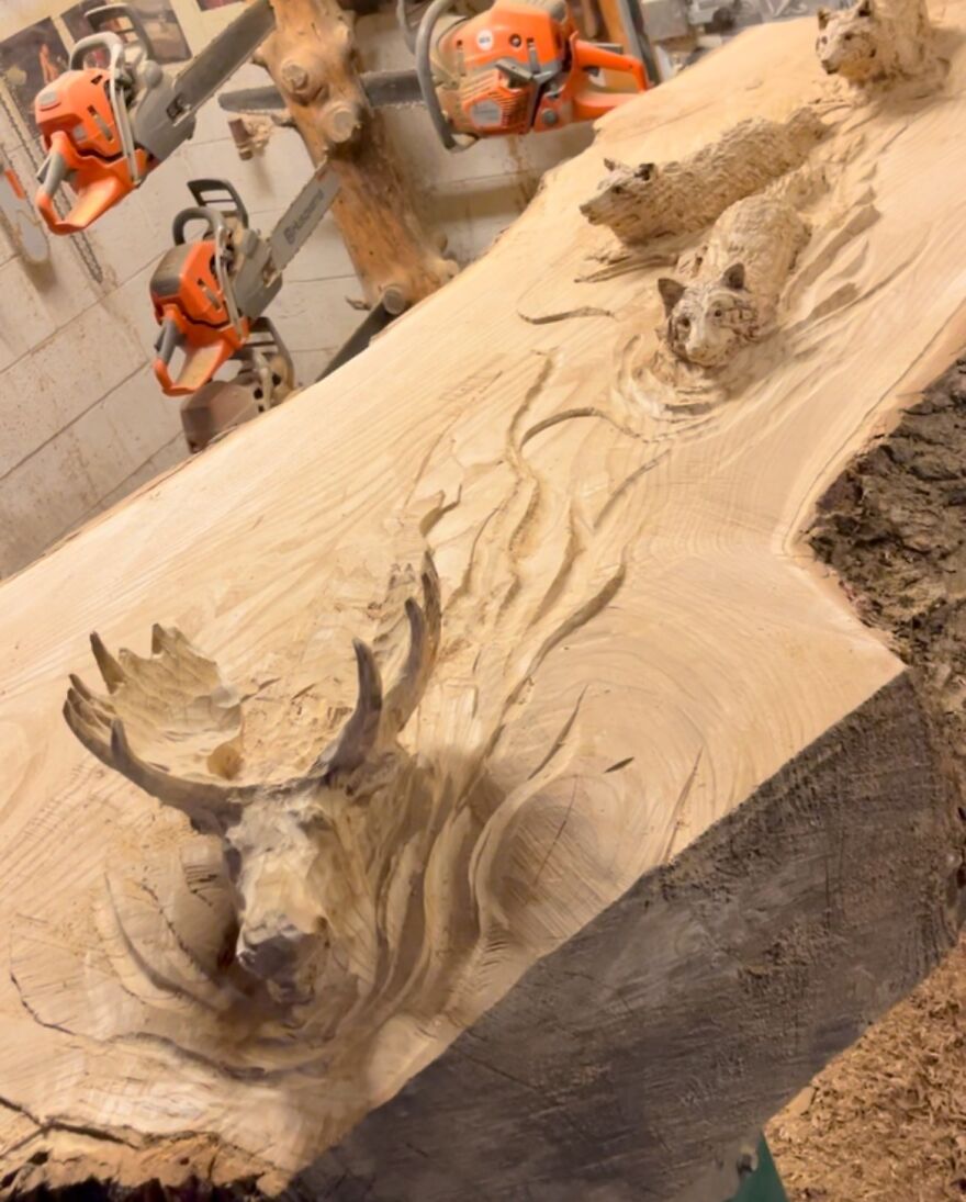 Chainsaw artist's intricate log sculpture featuring detailed animal carvings in a workshop setting.