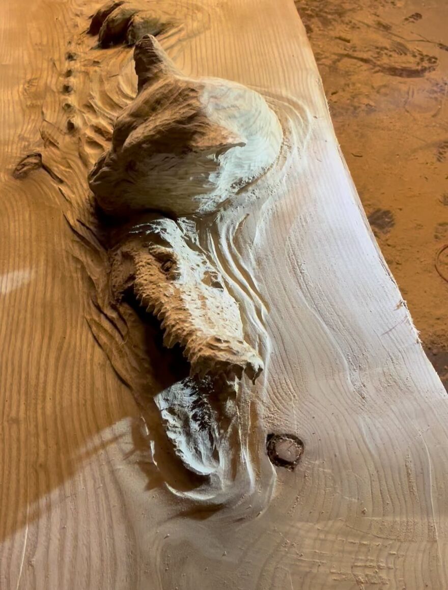 Chainsaw artist's intricate wood sculpture resembling a crocodile emerging from a log.