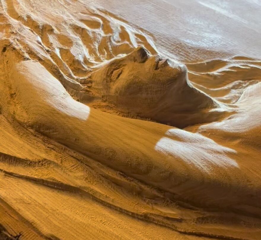 Chainsaw artist crafts a detailed sculpture of a reclining figure from a log.