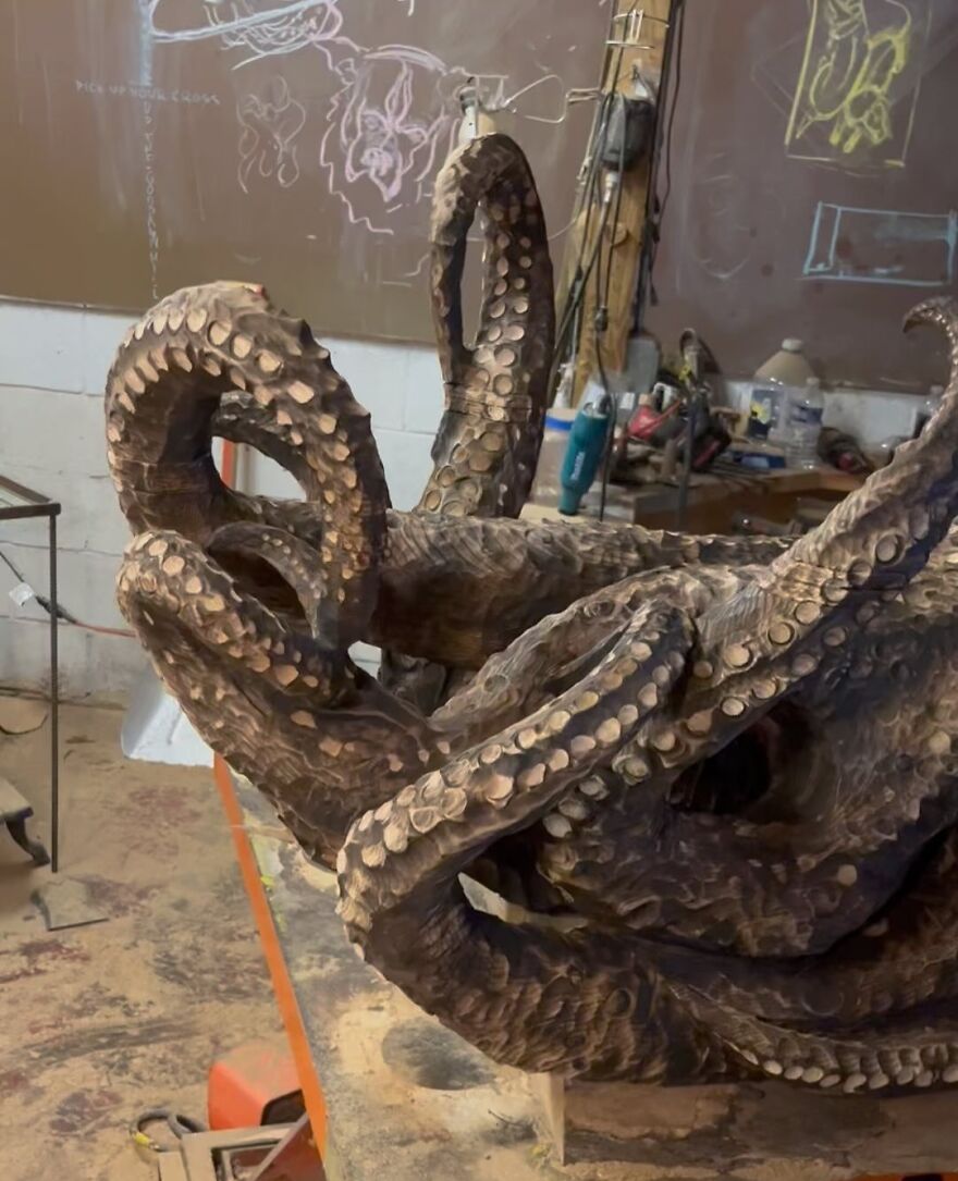 Chainsaw artist creates an intricate sculpture of octopus tentacles from a log in a workshop setting.