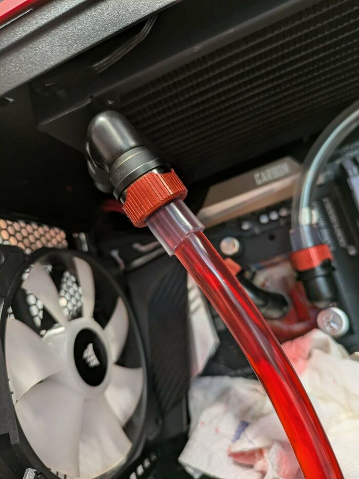 Close-up of a PC water cooling system with red coolant tubing and a white Corsair fan inside a computer case.