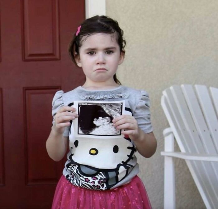 Young girl in a Hello Kitty shirt holding an ultrasound photo, an awkward family photo that feels incredibly sweet.
