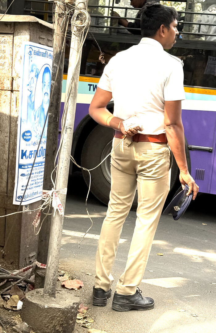 Man standing next to a pole with a mobile phone charger cable wrapped around his arm on a city street.