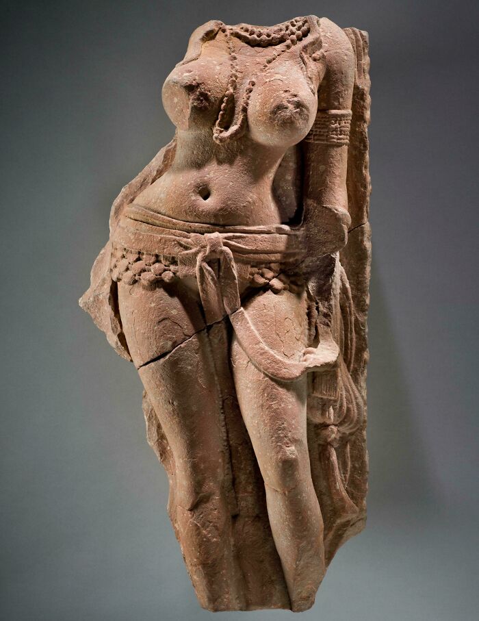Ancient artefact sculpture of a torso adorned with jewelry, showcasing intricate carvings.
